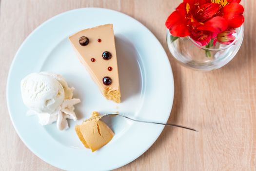 A piece of delicious caramel cheesecake served with ice cream and flowers on the table