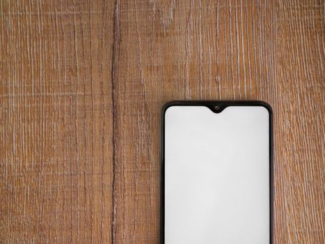 Black mobile smartphone mockup lies on the surface with blank screen isolated on wooden background. Top view flat lay with copy space, cut in the middle.