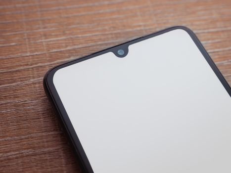 Black mobile smartphone mockup lies on the surface with blank screen isolated on wooden background. Top view closeup with selective focus and copy space, cut in the middle.