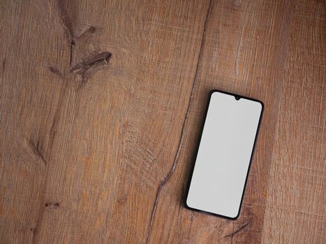 Black mobile smartphone mockup lies on the surface with blank screen isolated on wooden background. Top view flat lay with copy space.
