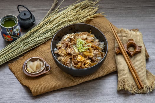 Japanese pork rice bowl with egg and onion (Donburi) served with pickled ginger and green tea on wooden table. Japanese food style.