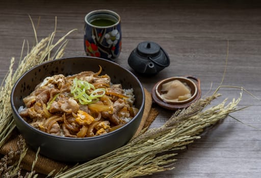 Japanese pork rice bowl with egg and onion (Donburi) served with pickled ginger and green tea on wooden table. Japanese food style.