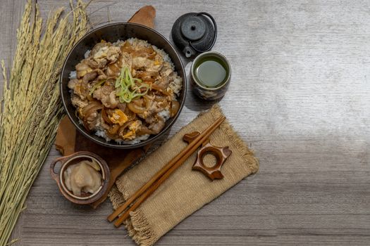 Japanese pork rice bowl with egg and onion (Donburi) served with pickled ginger and green tea on wooden table. Japanese food style.