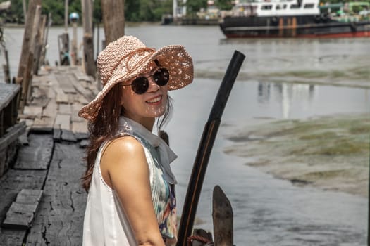 The girl in casual clothes are sitting smiling happily on the old wooden pier by the river. Personal holiday.