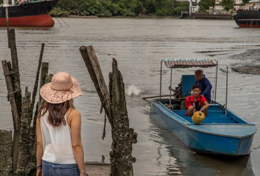 Bangkok, Thailand - 10 Jul, 2020 : Young woman in casual clothes standing on an old wooden pier waiting for ferryboat on the Chao Phraya River. Personal holiday.