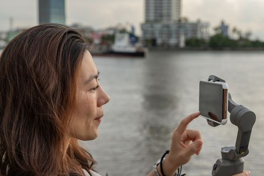 Side view of young woman standing by river and filming vdo on smartphone. Filming or shooting concept.