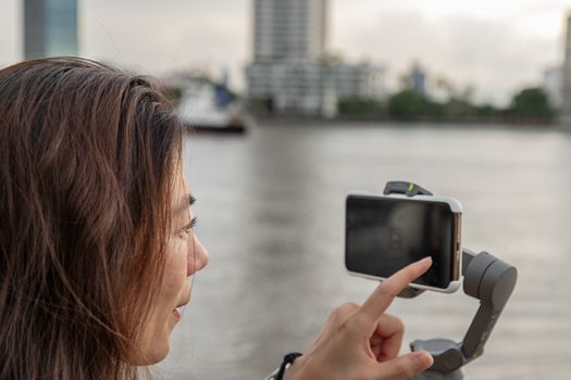 Side view of young woman standing by river and filming vdo on smartphone. Filming or shooting concept.