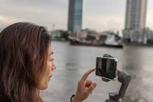 Side view of young woman standing by river and filming vdo on smartphone. Filming or shooting concept.