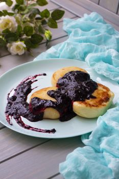 Cottage cheese pancakes with currant and blubbery jam on vintage teal plate, vertical image