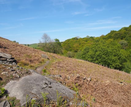 a narrow grass path on high rocky moorland above crimsworth dean valley and hardcaslte crags forest in west yorkshire