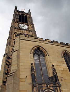 view of the clock tower and building of the historic saint peters parish church in the center of huddersfield against a cloudy sky