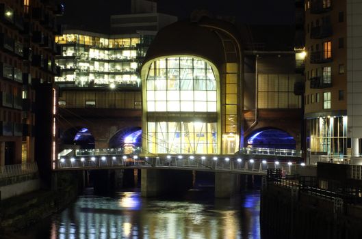 a cityscape night view of leeds showing the river aire running under the dark arches and the southern entrance to the station surrounded by illuminated office developments