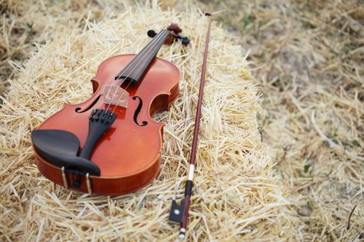 One violin and bow placed on a pile of straw in the field. Music Violin training. Fiddlestick, performing. Concept, baroque. Musical, fiddle.