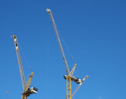 two tall yellow construction cranes working against a blue sky