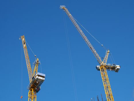 two tall yellow tower cranes working on a construction site against a blue sky