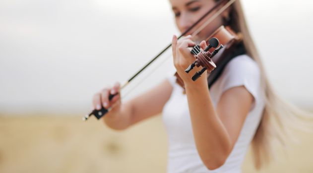 Beautiful romantic girl with loose hair playing the violin in the field after the harvest. Square sheaves of hay in the field. Violin training