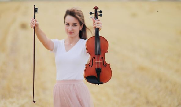 Beautiful romantic girl with loose hair playing the violin in the field after the harvest. Square sheaves of hay in the field. Violin training