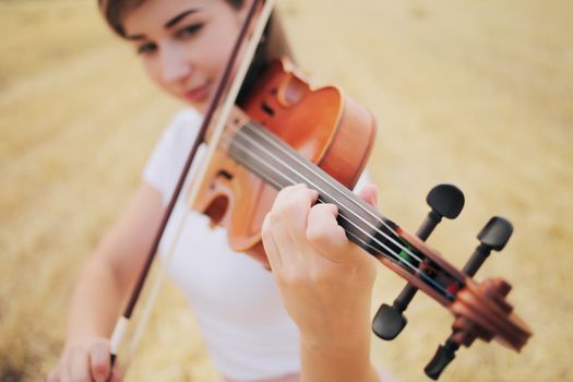 Beautiful romantic girl with loose hair playing the violin in the field after the harvest. Square sheaves of hay in the field. Violin training