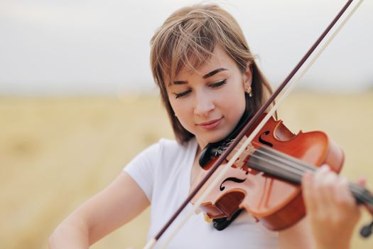 Beautiful romantic girl with loose hair playing the violin in the field after the harvest. Square sheaves of hay in the field. Violin training