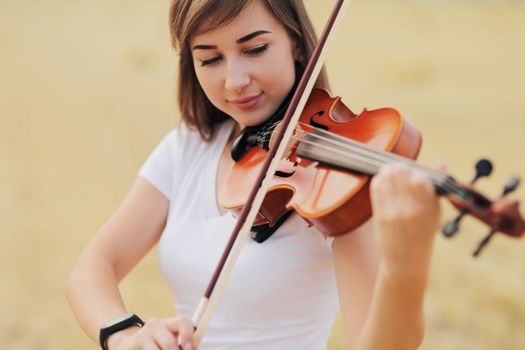 Beautiful romantic girl with loose hair playing the violin in the field after the harvest. Square sheaves of hay in the field. Violin training