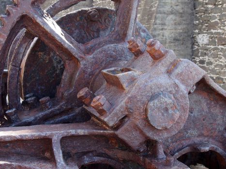 close up of an axle and broken spoked wheel on old rusted abandoned industrial machinery against a stone wall