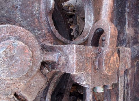 a close up of rusted iron connecting rods and gears with bolts on old corroded machinery