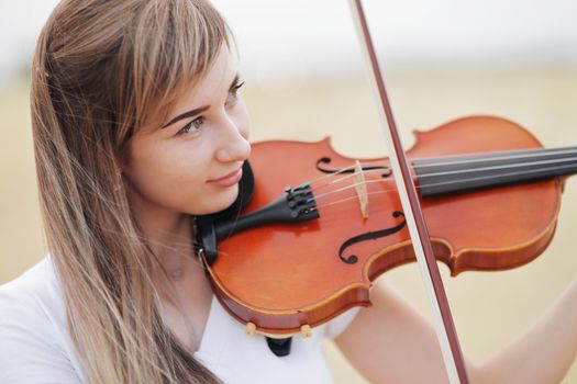 Beautiful romantic girl with loose hair playing the violin in the field after the harvest. Square sheaves of hay in the field. Violin training