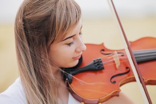 Beautiful romantic girl with loose hair playing the violin in the field after the harvest. Square sheaves of hay in the field. Violin training