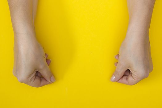 Hands with clenched fingers in a pinch on a yellow background