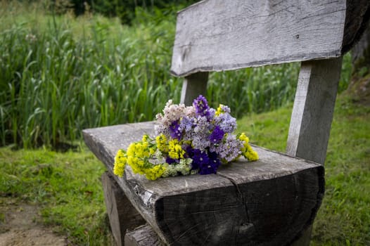 Posy of fresh spring flowers on a rustic weathered wooden bench outdoors in a park with a background of greenery conceptual of the season