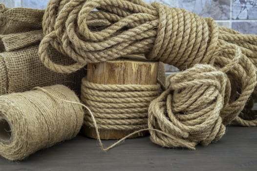 Jute rope and spools of burlap threads or jute twine in close-up on rustic wooden background