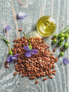 Flax seeds and flax oil. Brown linen seeds, flaxseed oil and blue flax flowers on old gray wooden background. Copy space. Top view or flat lay. Vertical.