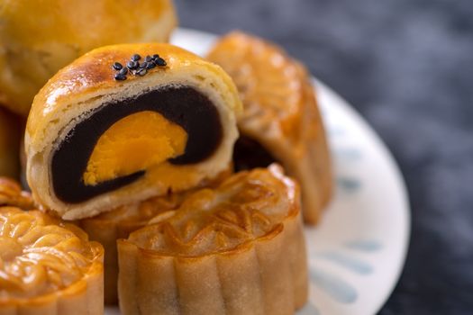 Tasty baked egg yolk pastry moon cake for Mid-Autumn Festival on black slate dark background. Chinese festive food concept, close up, copy space.