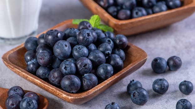 Pile of blueberry fruit in a bowl plate on a tray over gray cement concrete background, close up, healthy eating design concept.