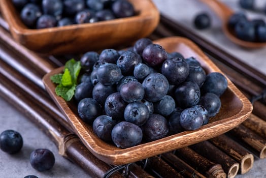 Pile of blueberry fruit in a bowl plate on a tray over gray cement concrete background, close up, healthy eating design concept.