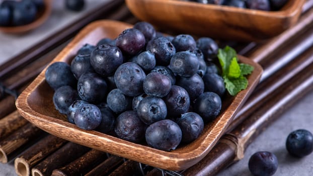 Pile of blueberry fruit in a bowl plate on a tray over gray cement concrete background, close up, healthy eating design concept.