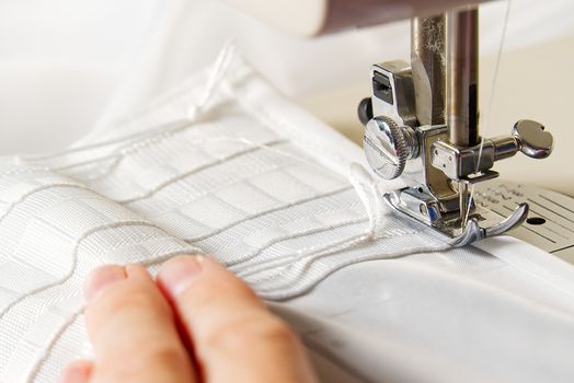 A woman works on a sewing machine. seamstress sews white curtains, close up view