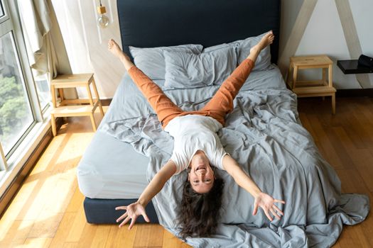 Beautiful young brunette girl fooling around on the bed. View from above. Good mood.