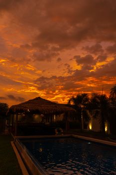 Beautiful orange fiery sunset in the tropics. Street canopy from hay, next to the pool and overlooking the rice field