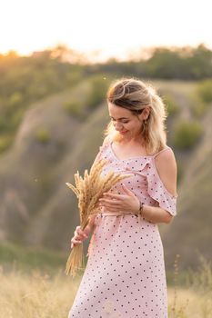 Beautiful tender girl in a white sundress walks at sunset in a field with a spikelet bouquet