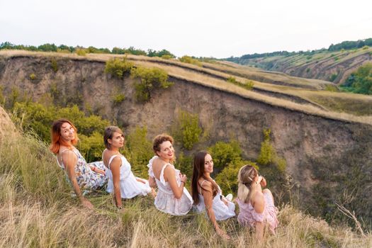 A cheerful company of beautiful girls friends enjoy a picturesque panorama of the green hills at sunset.