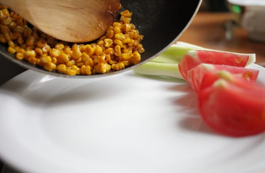 Diet. Organic Grilled Corn in a frying pan. Organic farm vegetables. Chopped tomato and cucumber on a white plate. Wooden spoon. Environmentally friendly products