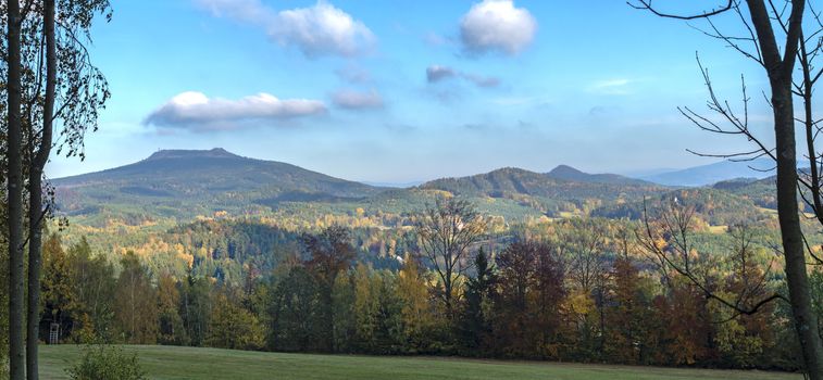 Luzicke hory panorama, meadow with autumn colorful forest and trees and hills with lookout tower on hill Hochwald Hvozd and blue sky landscape in luzicke hory mountain