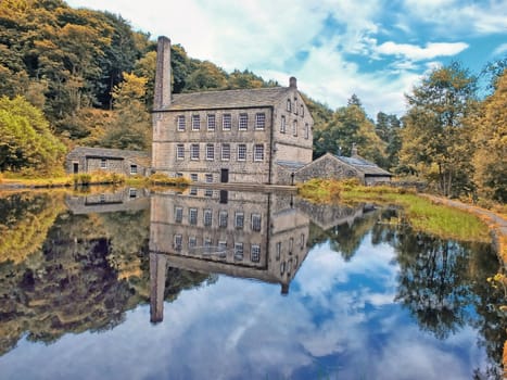 gibson mill a water powered mill with main bulding relected in the pond and surroounding trees of hardcastle crags near hebden bridge in west yorkshire