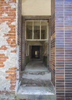 View from entrance door to interior of an abandoned ruined building of house, ruins with empty corridor, broken windows, doors and bricks, vertical symmetrical view.