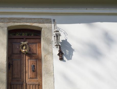 old rustic wooden door with sandstone lining, wreath, lantern and cross on white wall background, copy space