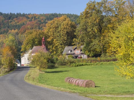 road to the village chapel in autumn rural landscape with straw bales in luzicke hory mountain