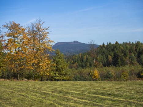 meadow with autumn colorful forest and trees and hills with lookout tower and blue sky landscape in luzicke hory mountain