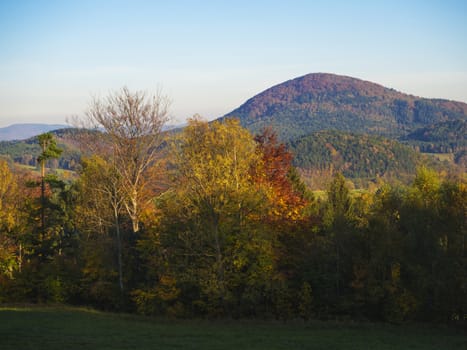 green meadow with autumn colorful forest and trees and hill and blue sky landscape in luzicke hory mountain