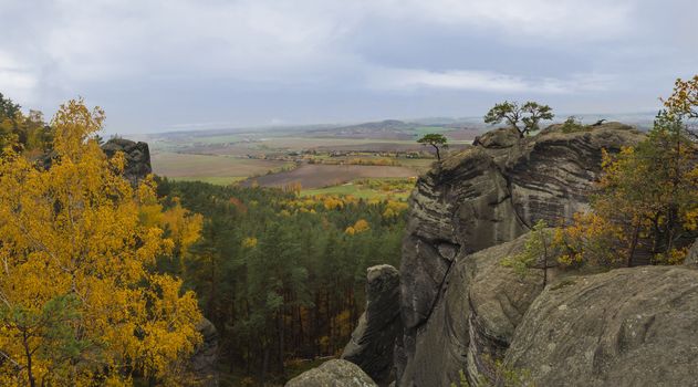 Panoramic view from sandstone pillars view-point at nature reserve Cesky Raj with autumn colored deciduous and coniferous tree forest and green hills, moody blue sky.
